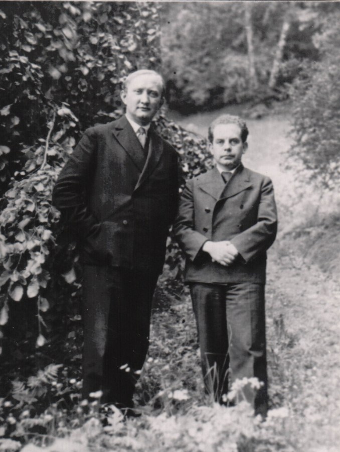 Karl König steht neben Emil Bock, der einen guten Kopf größer ist. Im Freien vor Bäumen. Schwarzweiß-Foto.