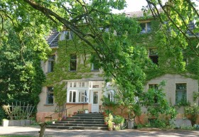 Das Wohnhaus in Altthymen ist eine alte beigefarbene Villa, im Vordergrunsd etwas verdeckt durch die grünen Zweige eines Baumes